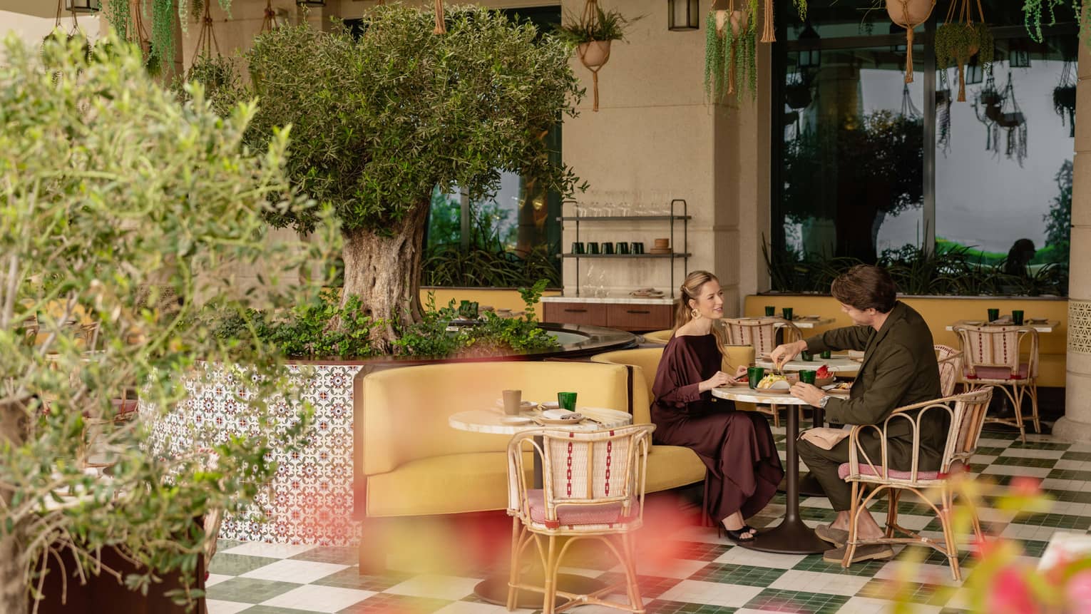 A couple dines at a colourful outdoor patio with green, checkered floors, mosaic tiles and lush greenery