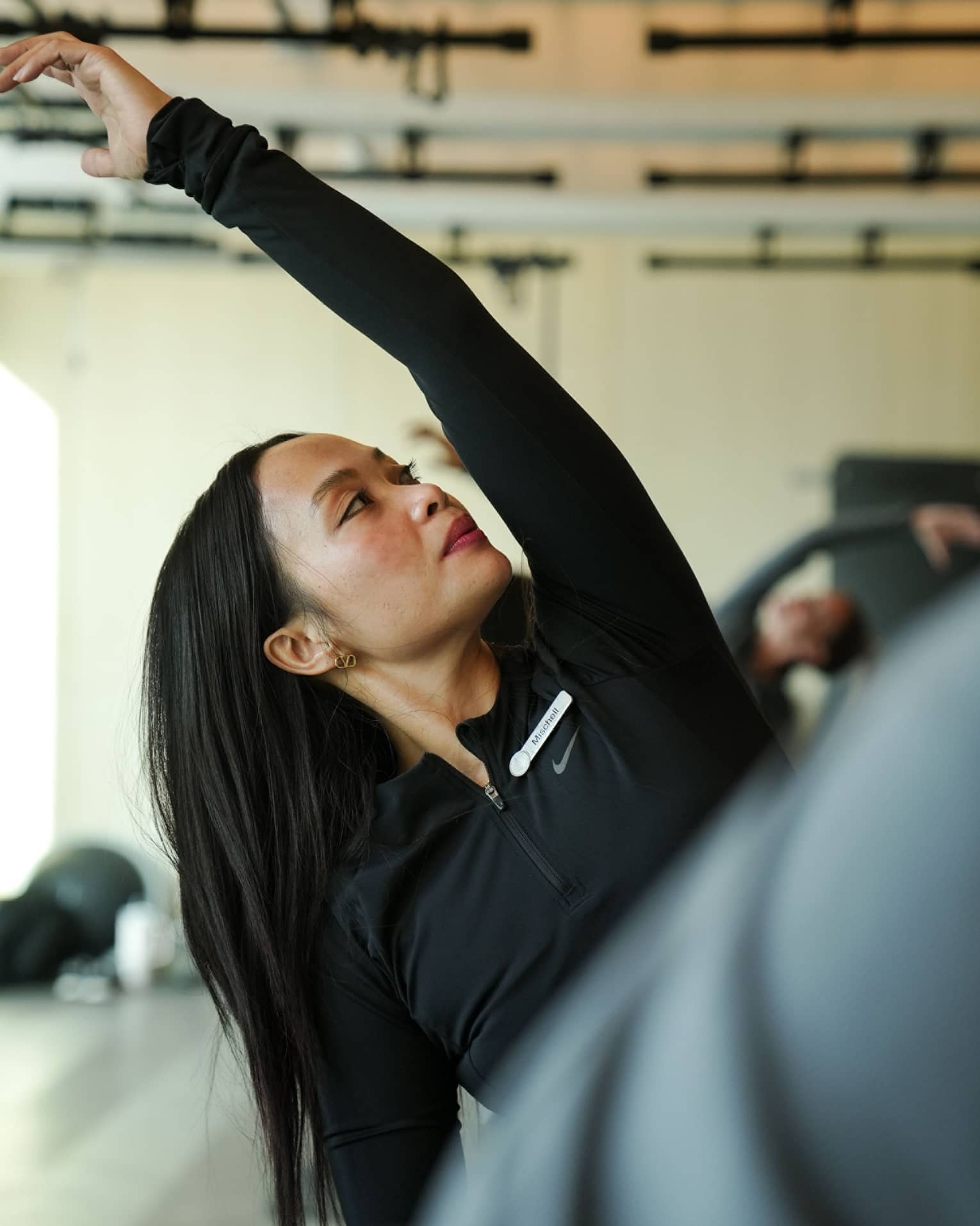 Person with long dark hair wearing black atheltic clothing stretches their arm over their head