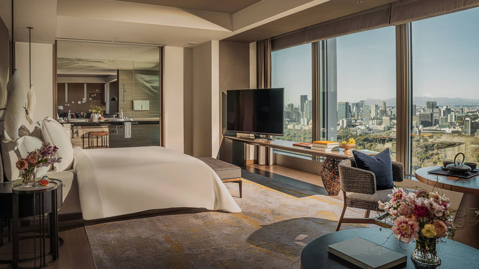 Luxury hotel suite featuring a king bed facing a wall of windows, plus a dining table