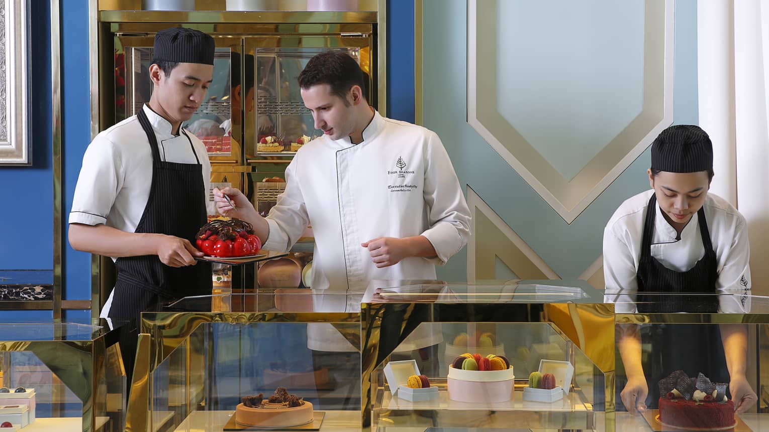 Three chefs with cakes, desserts at pastry counter 