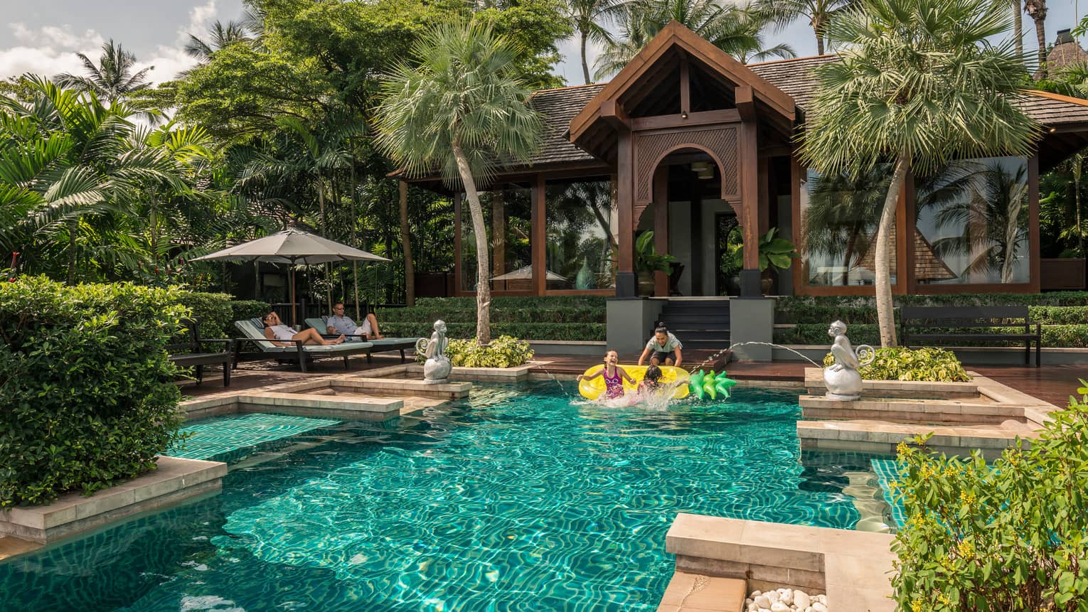 Family swims under monkey fountains in private residence outdoor swimming pool