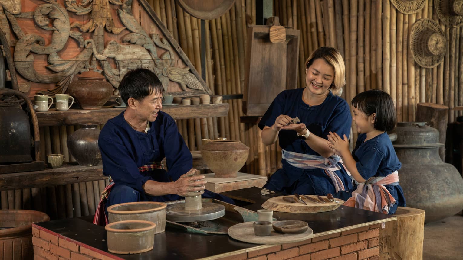 A potter teaching a woman and a child to shape clay in a rustic pottery workshop, surrounded by traditional tools and pottery.