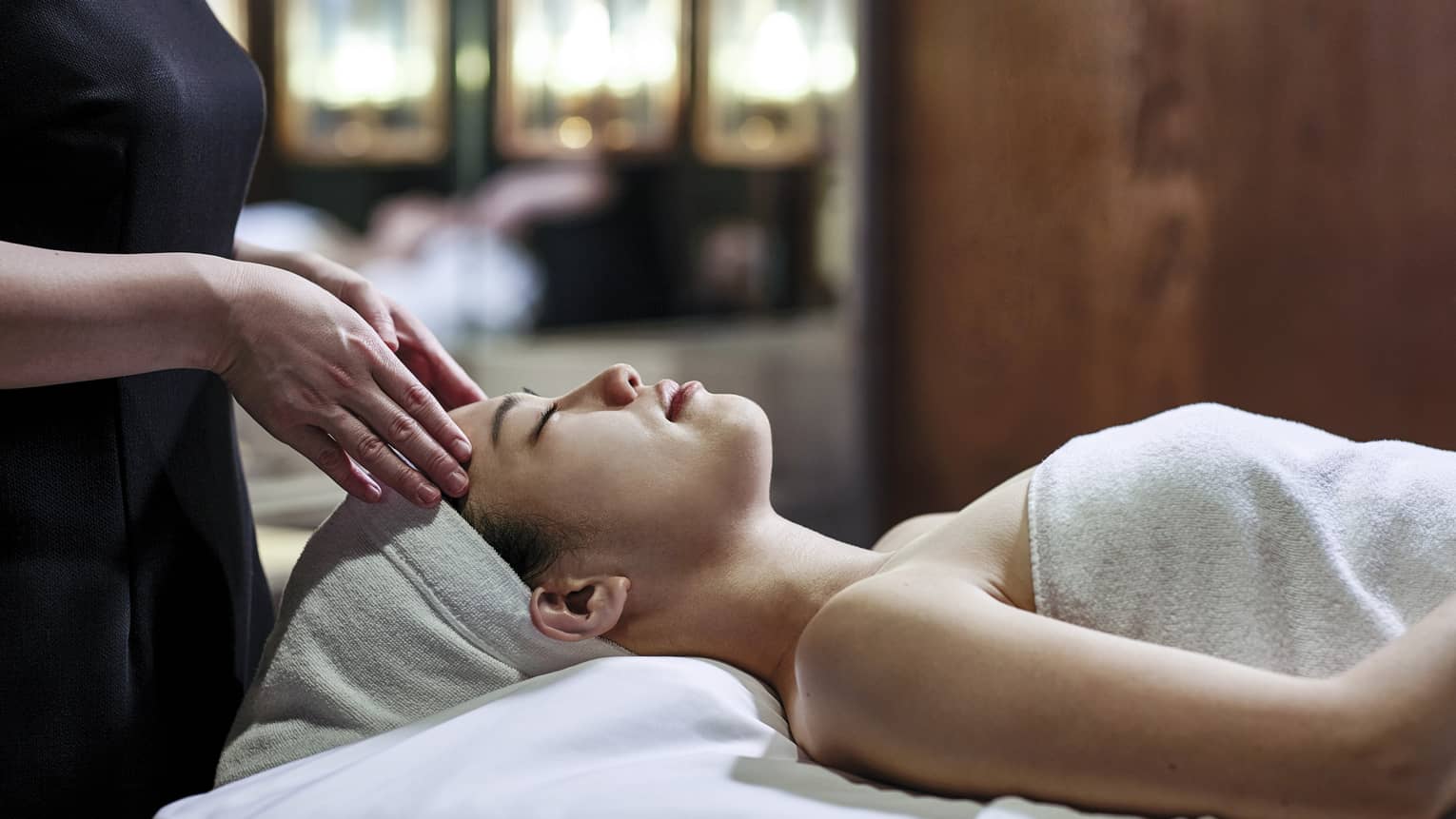 Woman getting a head massage during spa treatment, white towel over her and her head