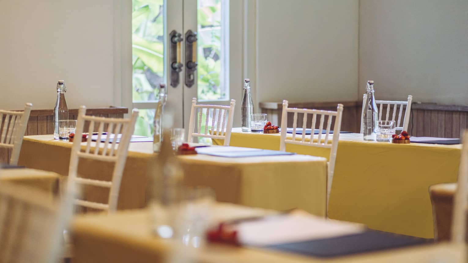 Tables with two white chairs, each with yellow table clothes, set for meeting