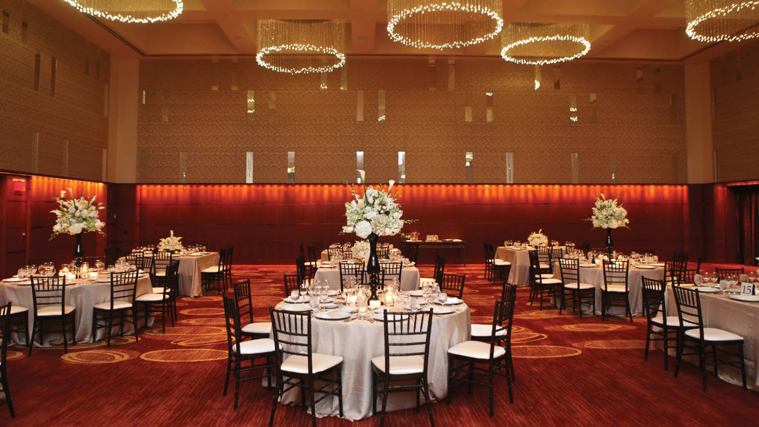 Intricate light fixtures hang above round tables with large flower bouquets and candles
