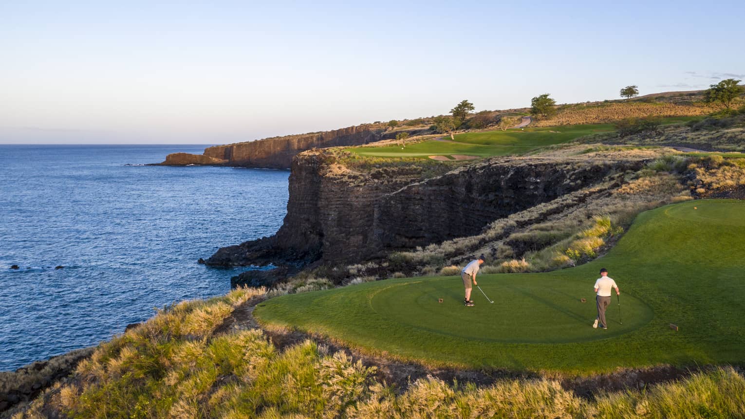 Two golfers at the 12th-hole tee at Manele Golf Course at Four Seasons Resort Lanai, cliffs and ocean in background