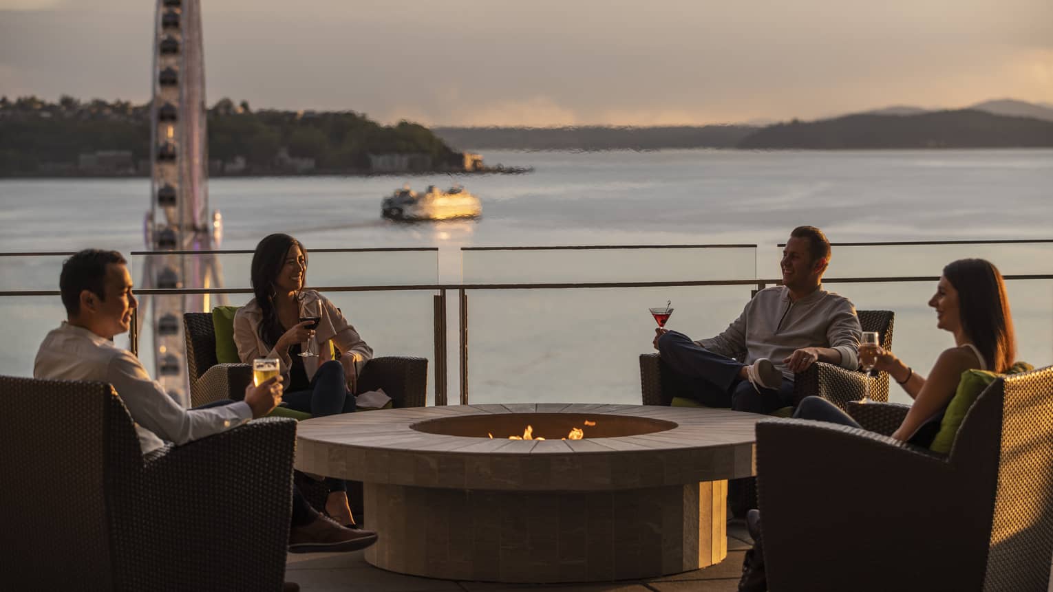 Guests enjoy drinks by the firepit with a view of the Seattle Great Wheel and bay behind them