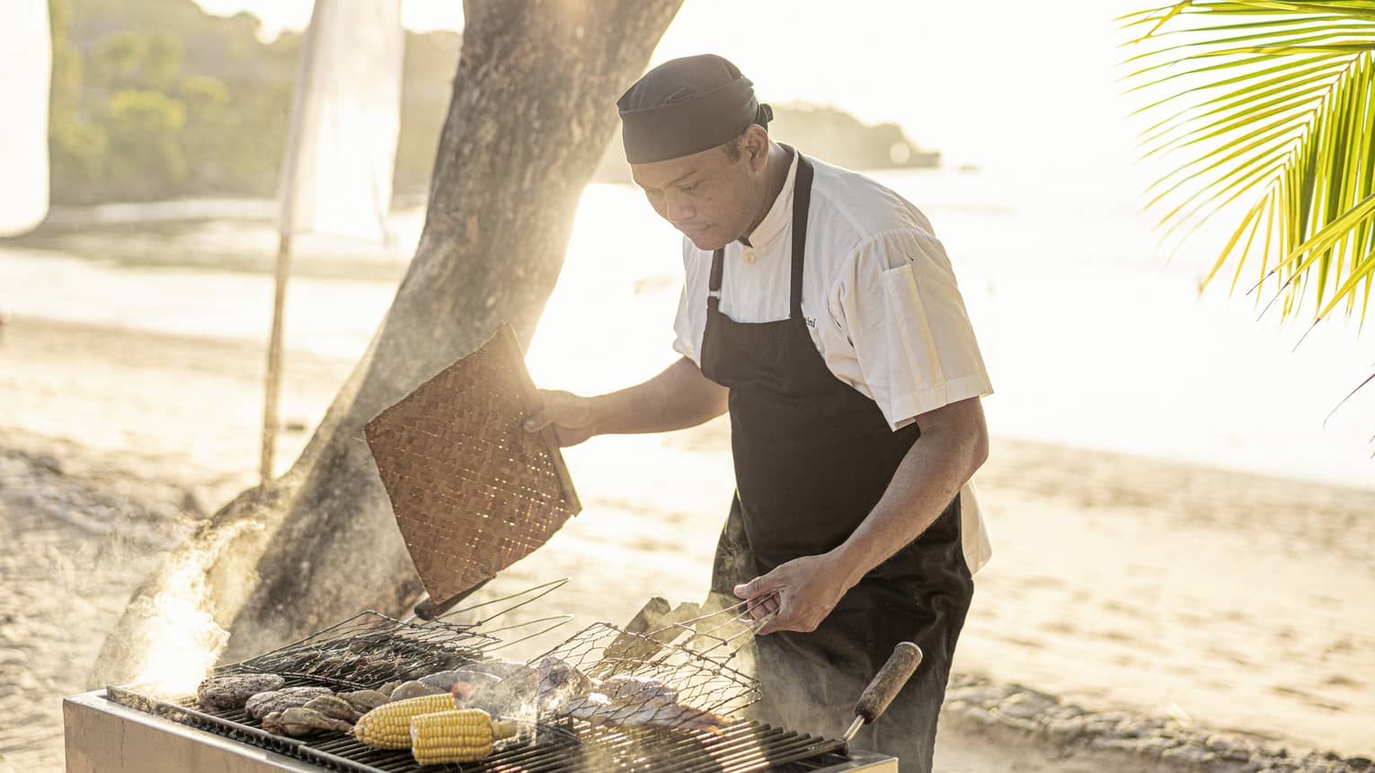 Chef grills fresh clams and corn on the cob over a beachside BBQ