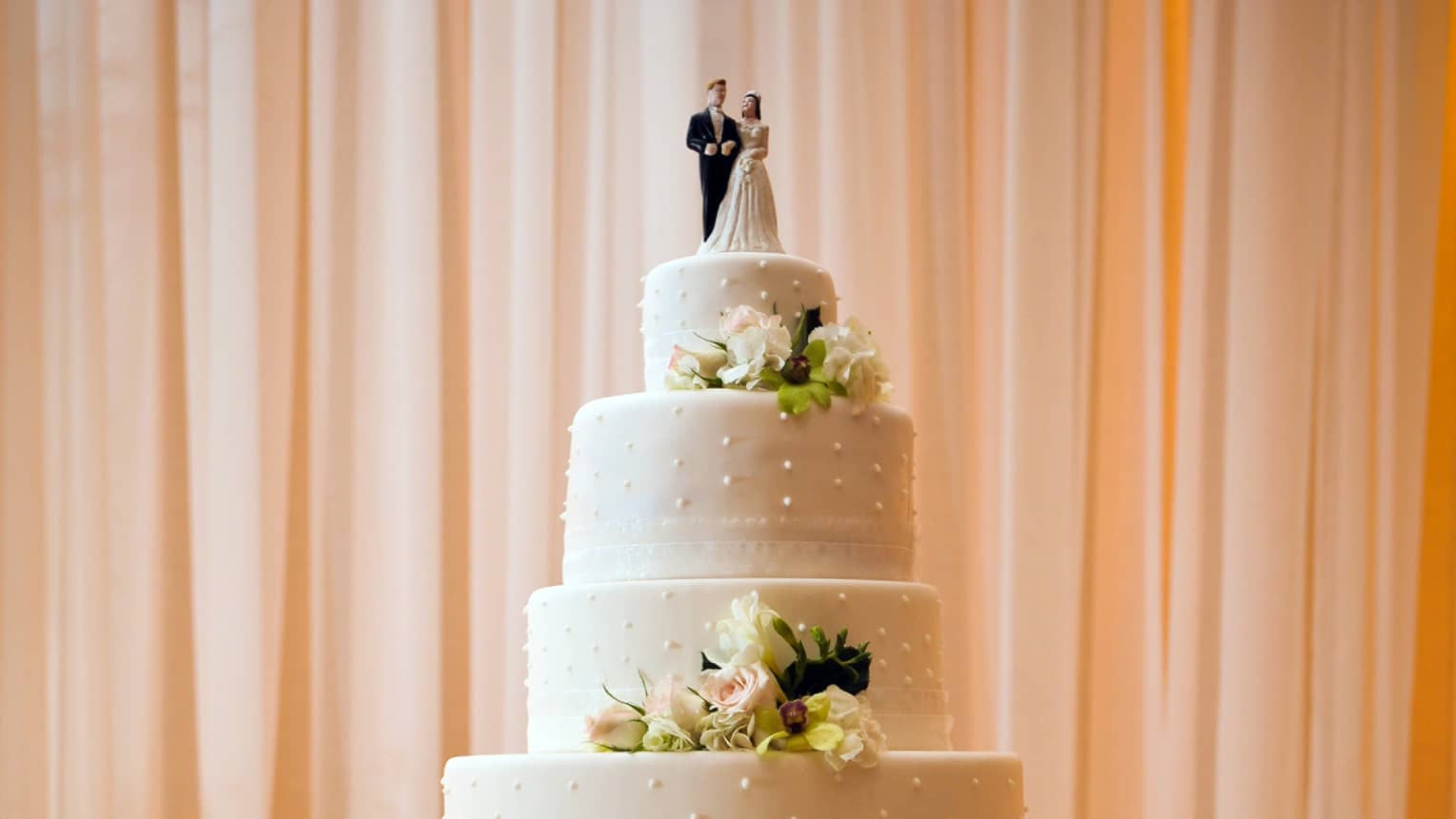 Six-tiered wedding cake on table with gold linen, tealight candles, white roses 