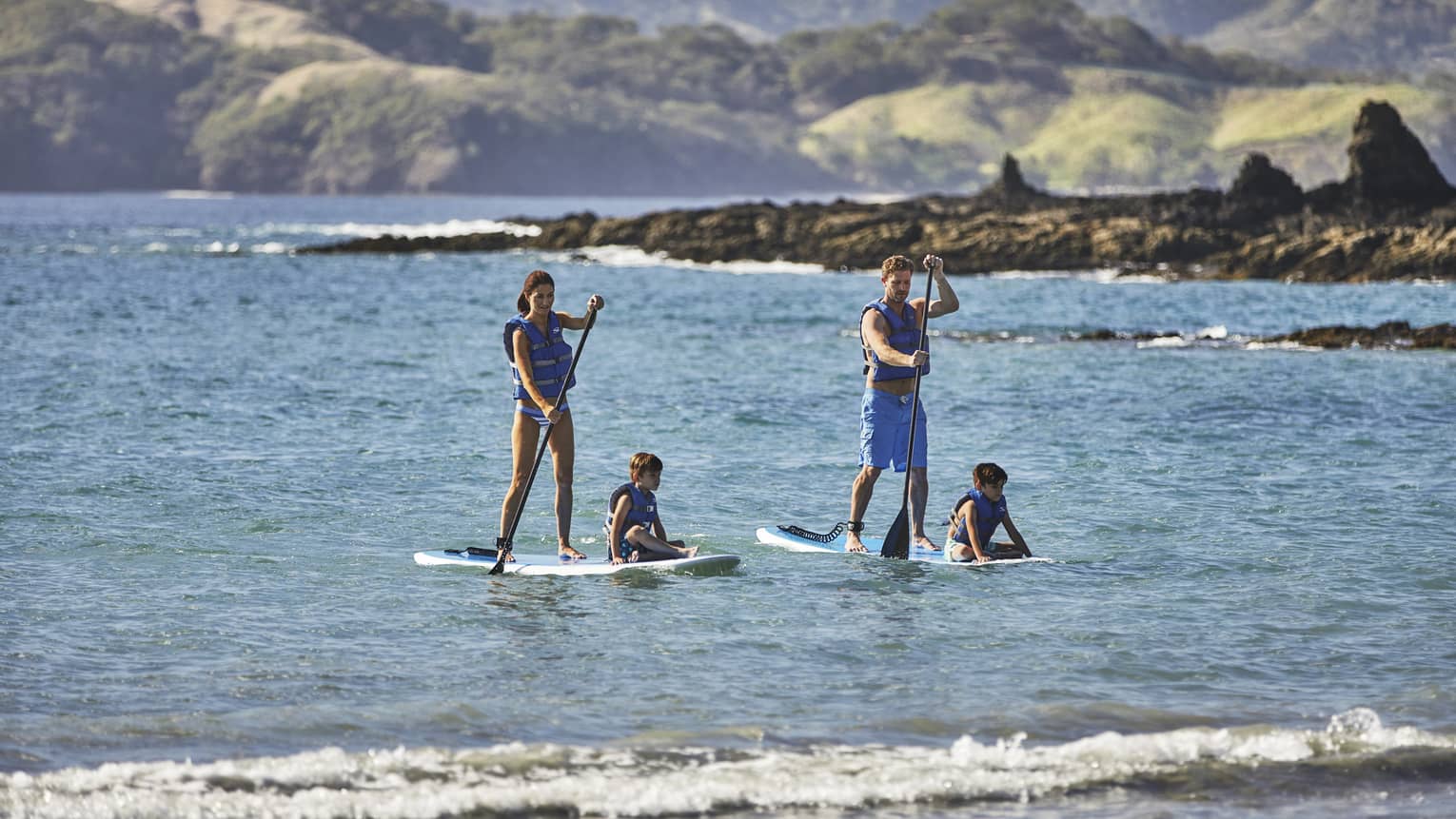 A family paddles into the surf with several archipelagos in the background.