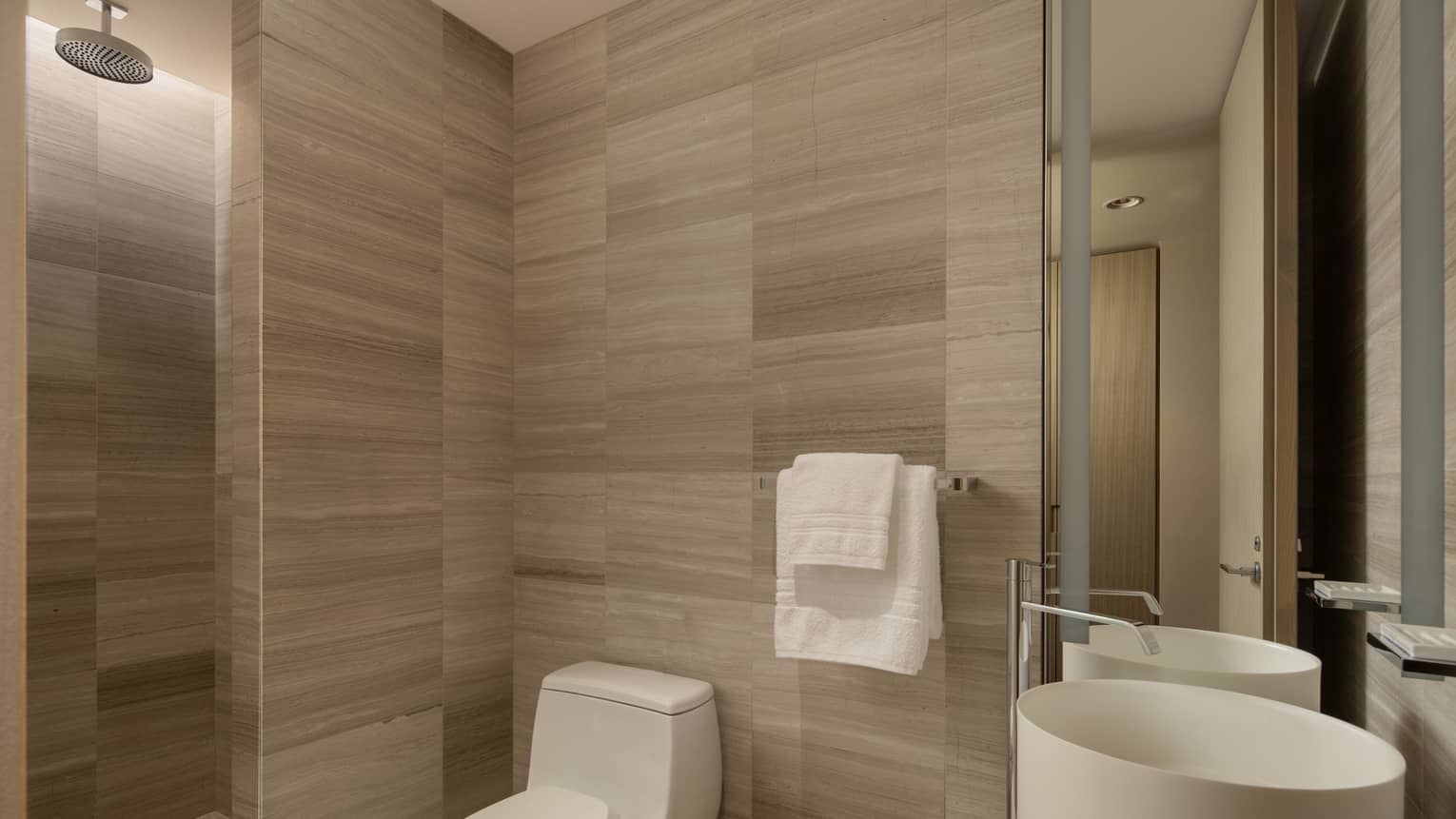 Hotel suite bathroom with a toilet, round sink, two towels on a rack and rain shower head 