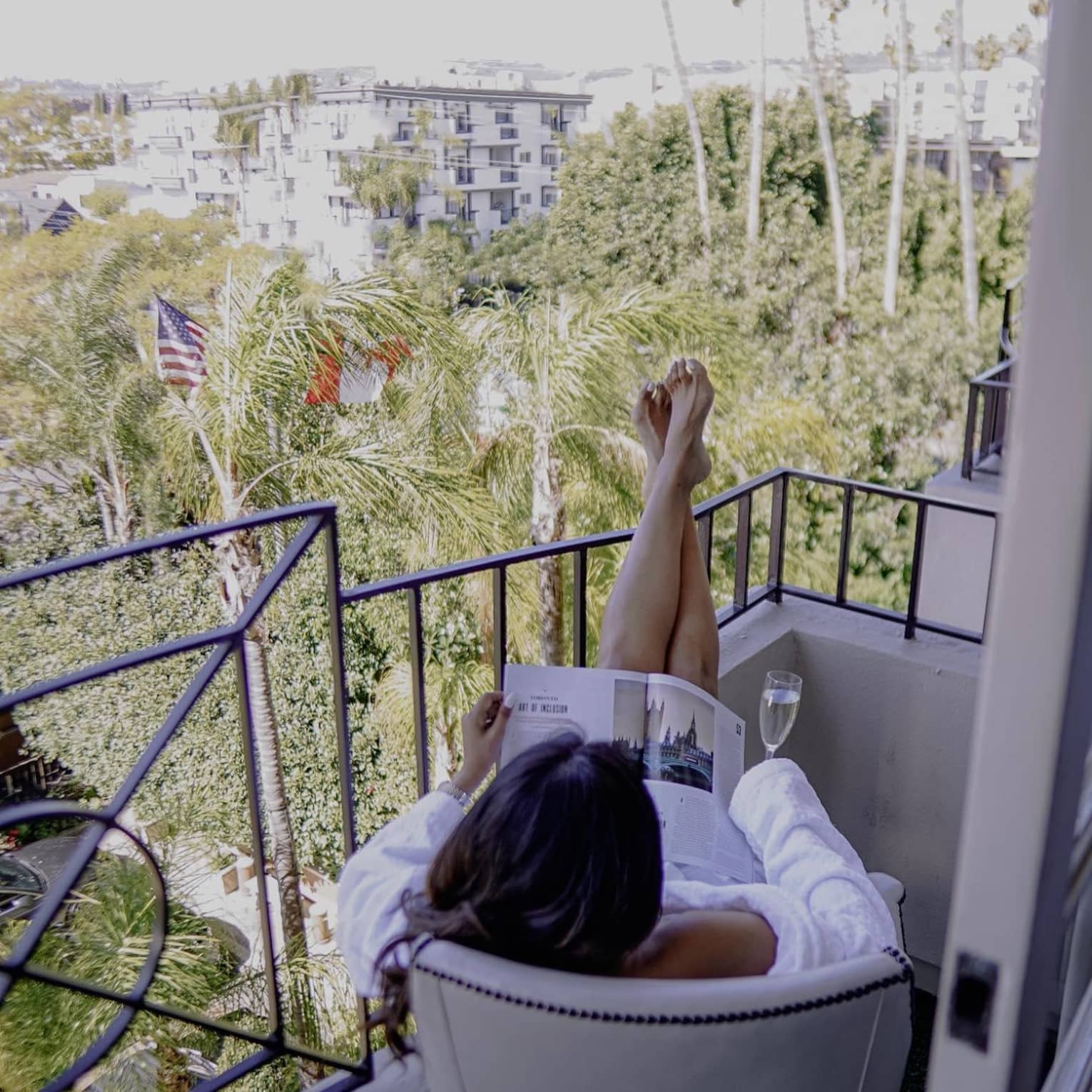 Woman sitting on balcony with champagne reading a magazine