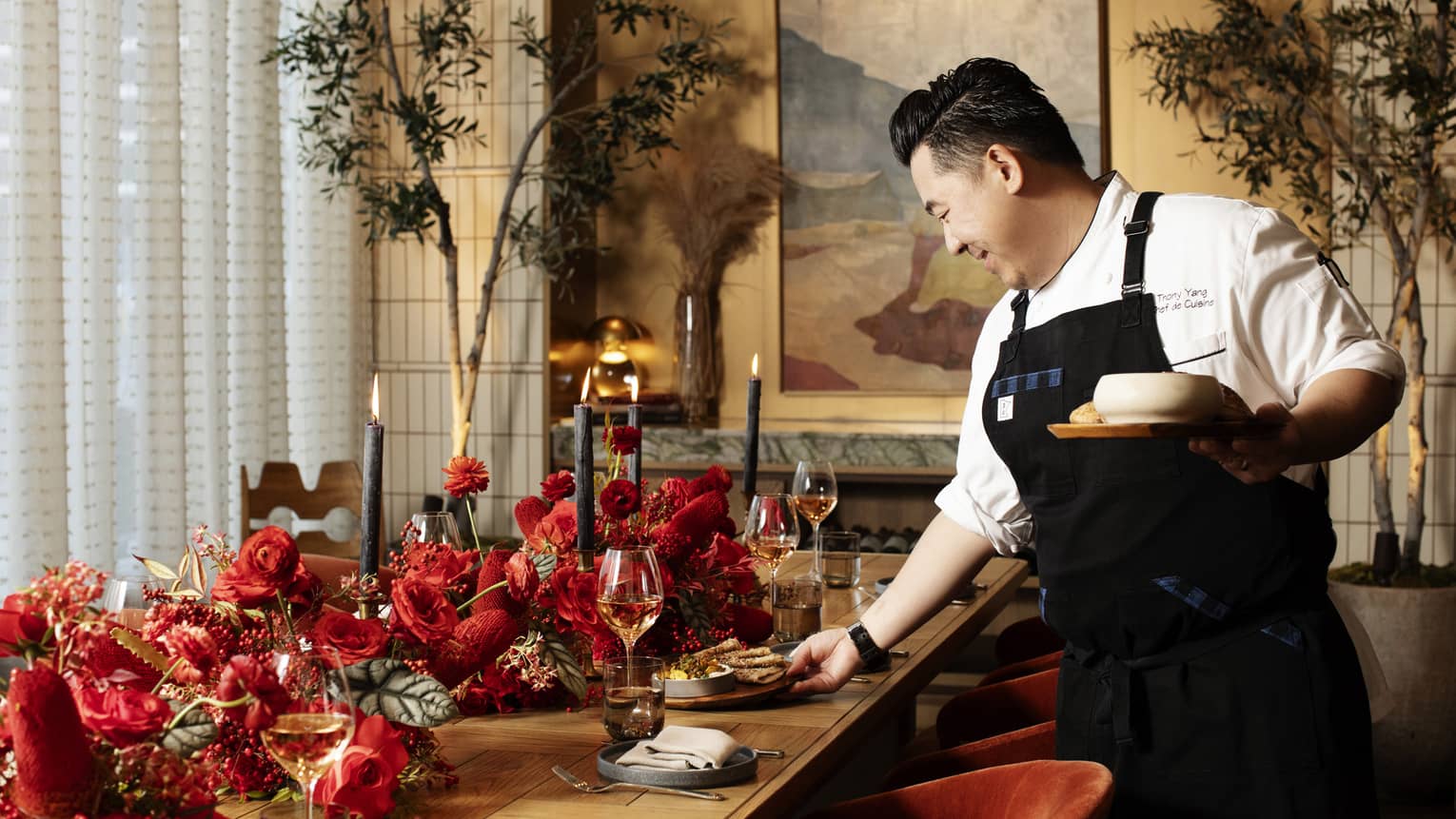Chef putting dishes on a table with red flowers on it.
