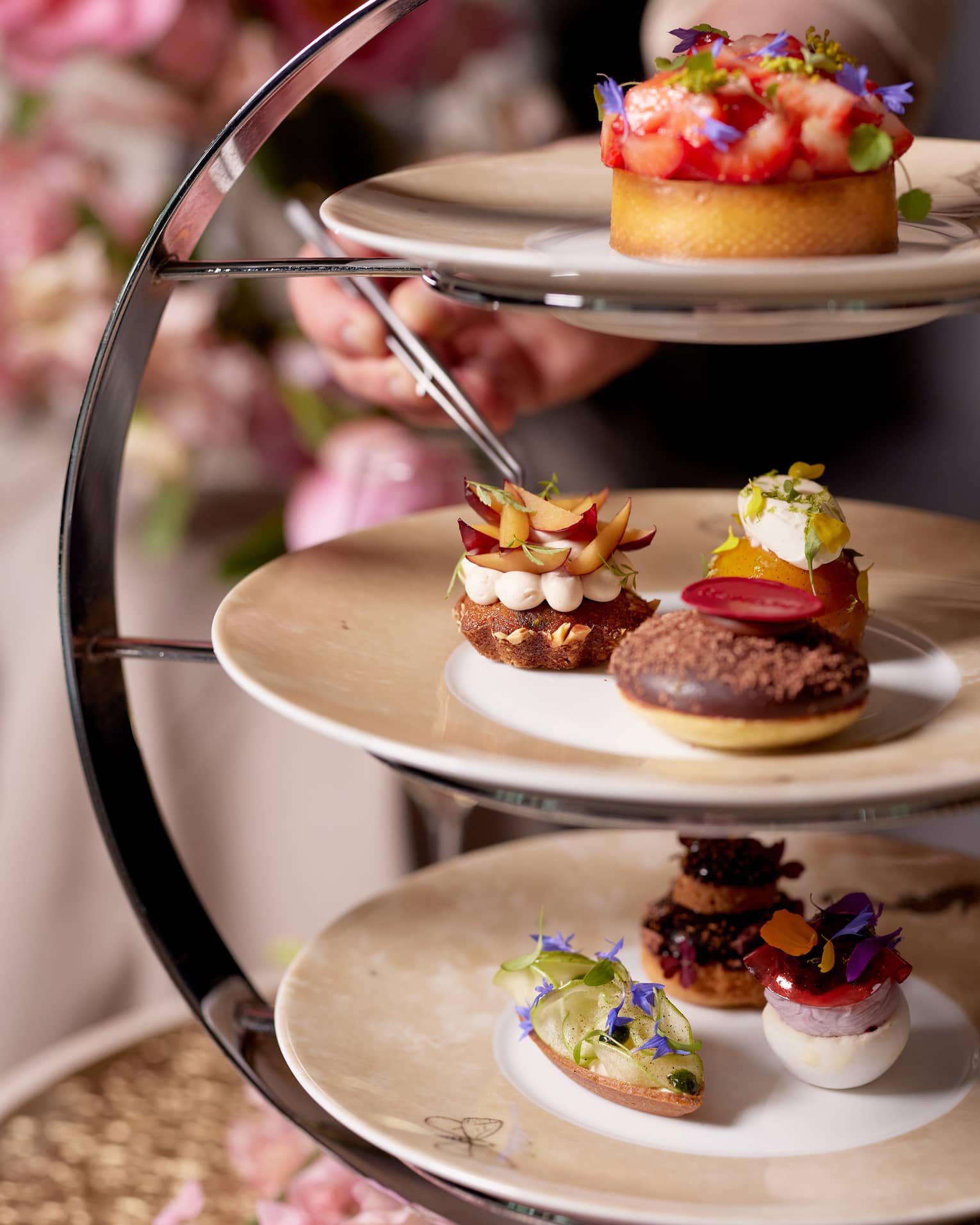 A close-up of a plate of three pastries topped variously with sliced fruit, chocolate, fresh herbs, cream and flower petals.