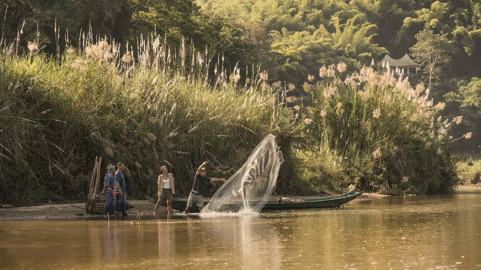 Man throws traditional Thai fishing net from boat into river during group activity