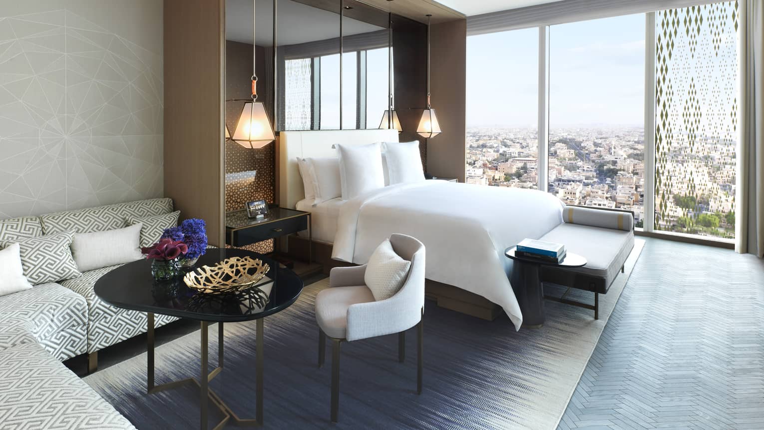 Hotel room L-shaped corner sofa, coffee table and chairs beside bed, wall of windows