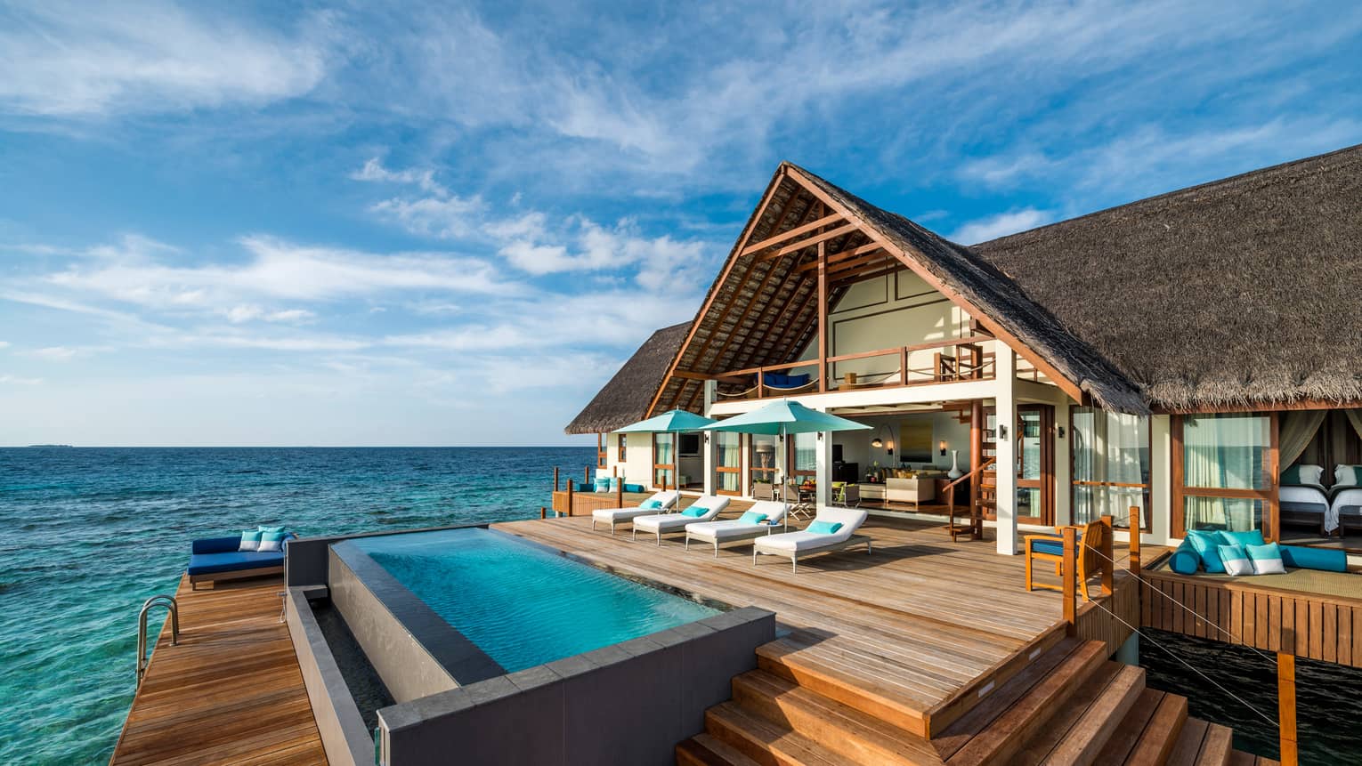 Sunset Two-Bedroom Water Suite with thatched roof, lounge chairs on large patio by pool