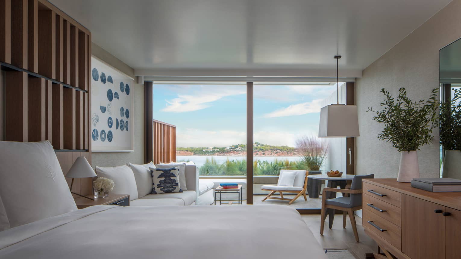 Hotel room with white king bed, modern wooden dresser and wooden accent wall, sofa, walk-out balcony