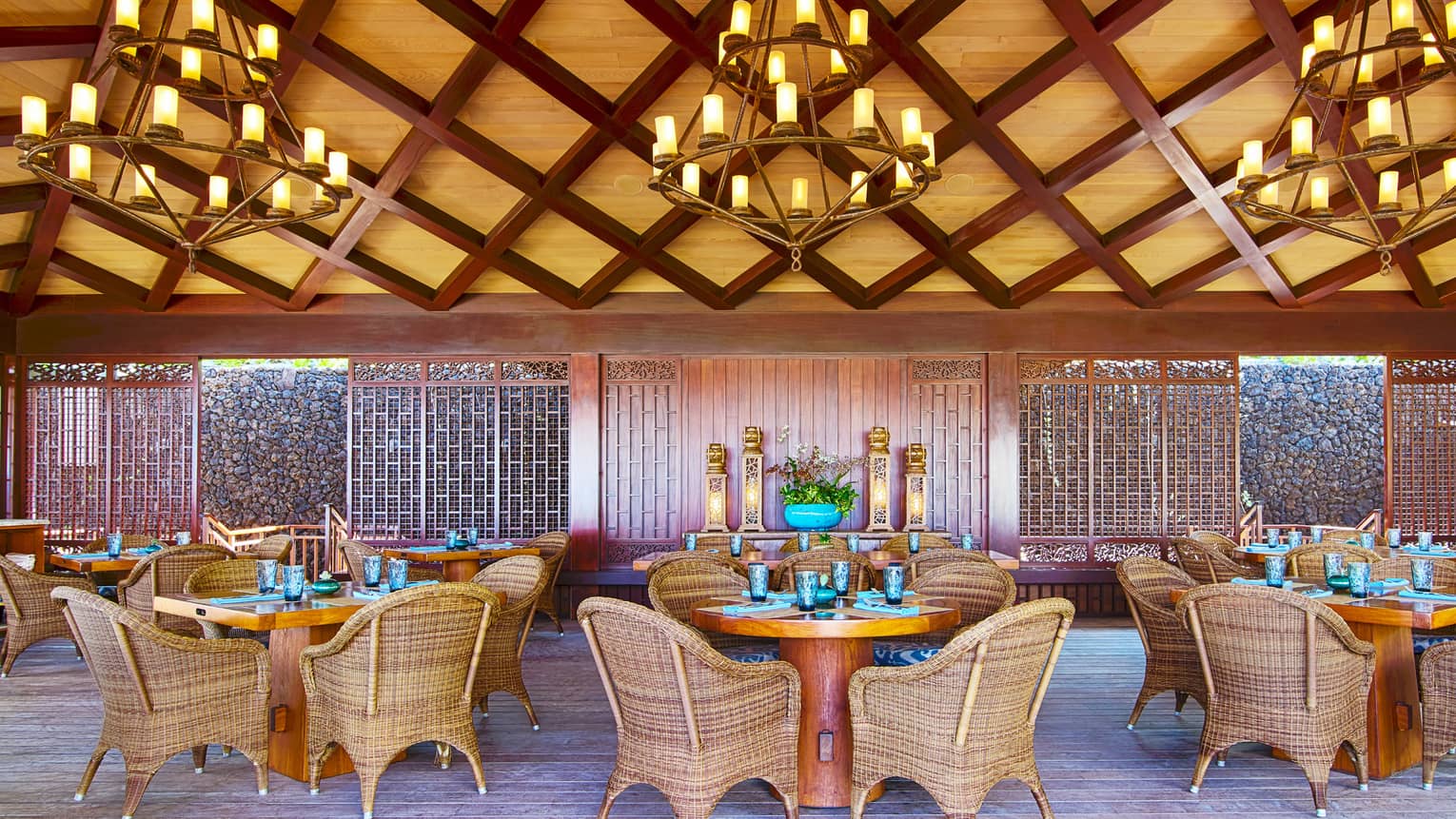 Dining area under bamboo and lattice ceiling with three chandeliers, round dining tables and wicker chairs