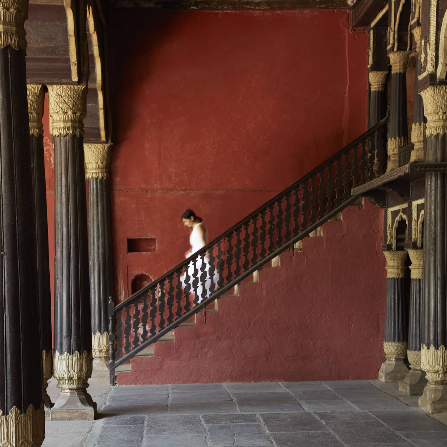 Side view of a guest descending a stone staircase, in a room supported by pillars with intricate gilded embellishments.