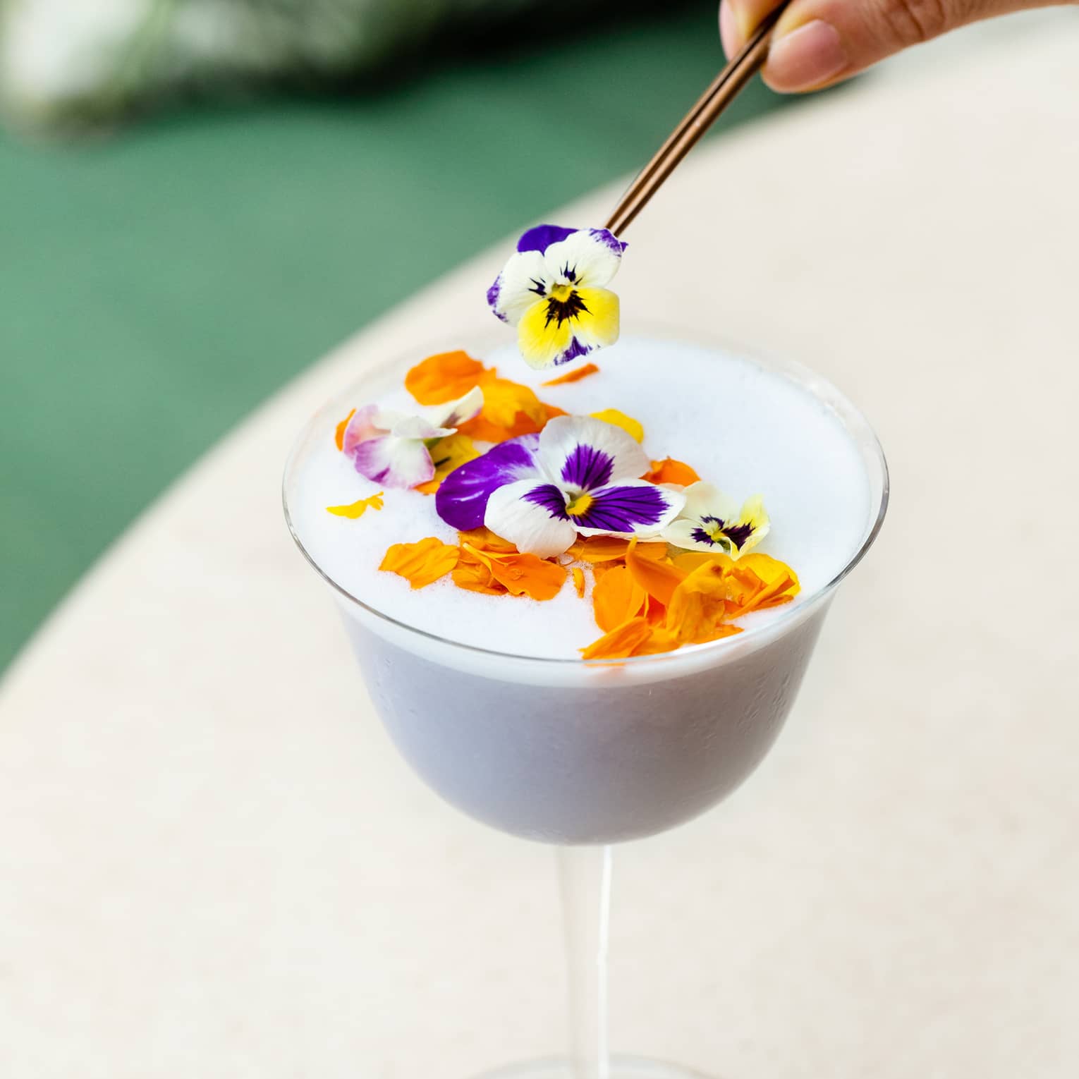 A stemmed glass of a white tropical cocktail topped with flowers 