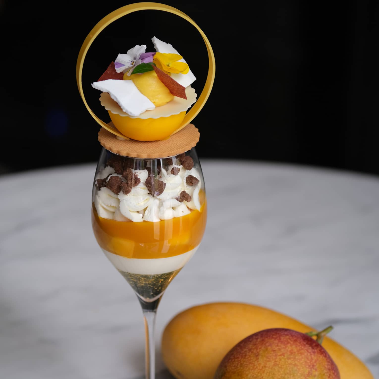 Two mangos beside a glass of a mango parfait