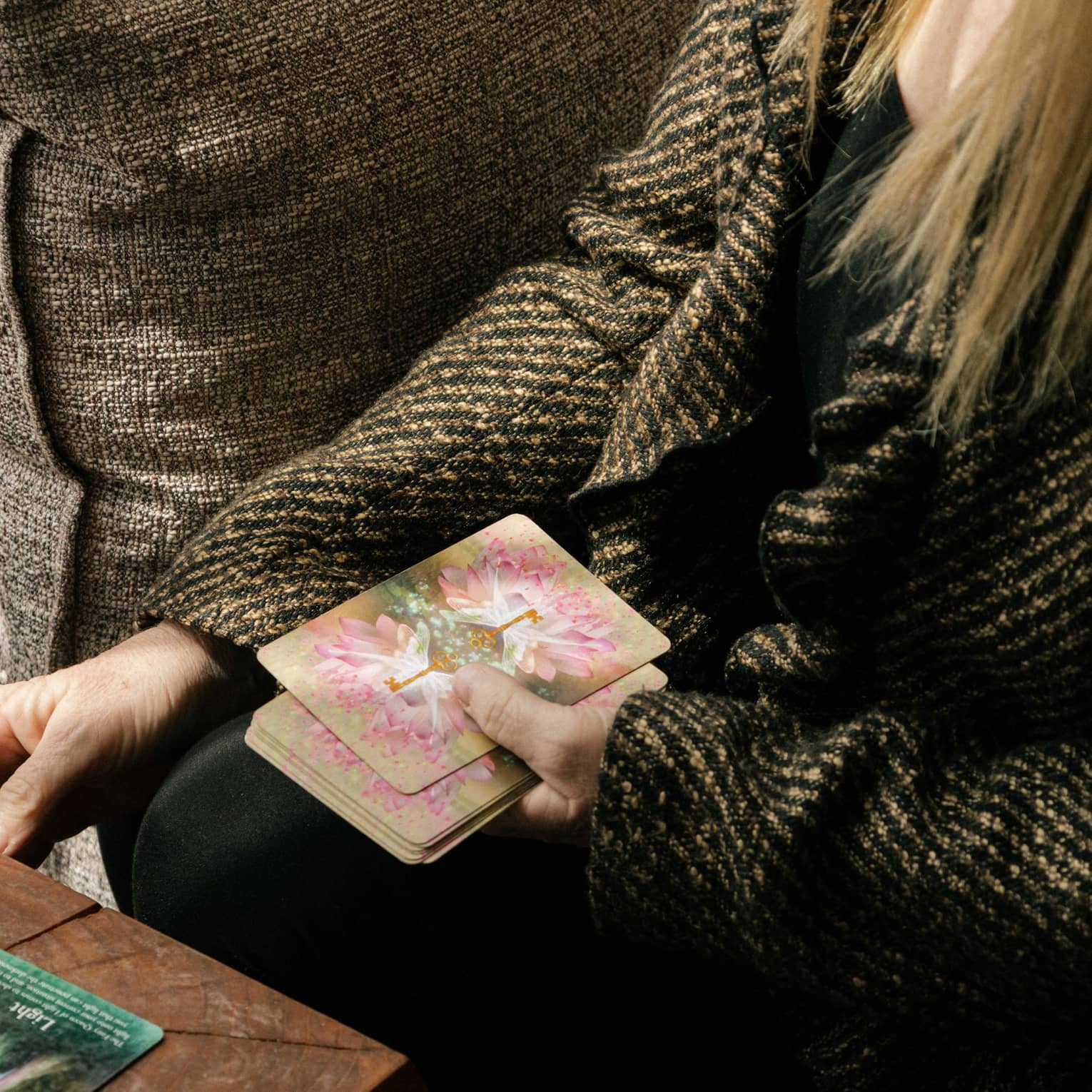 Person wearing tweed jacket draws a card onto a table during a spiritual card reading session