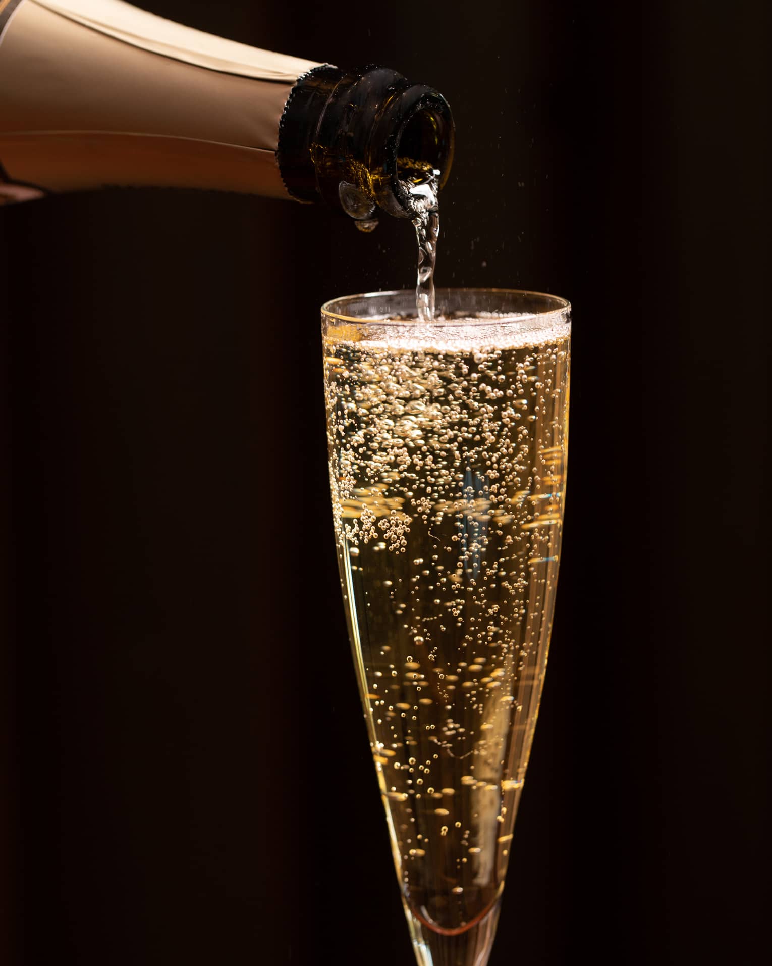 A bottle of champagne is poured into a glass as bubbles float to the top