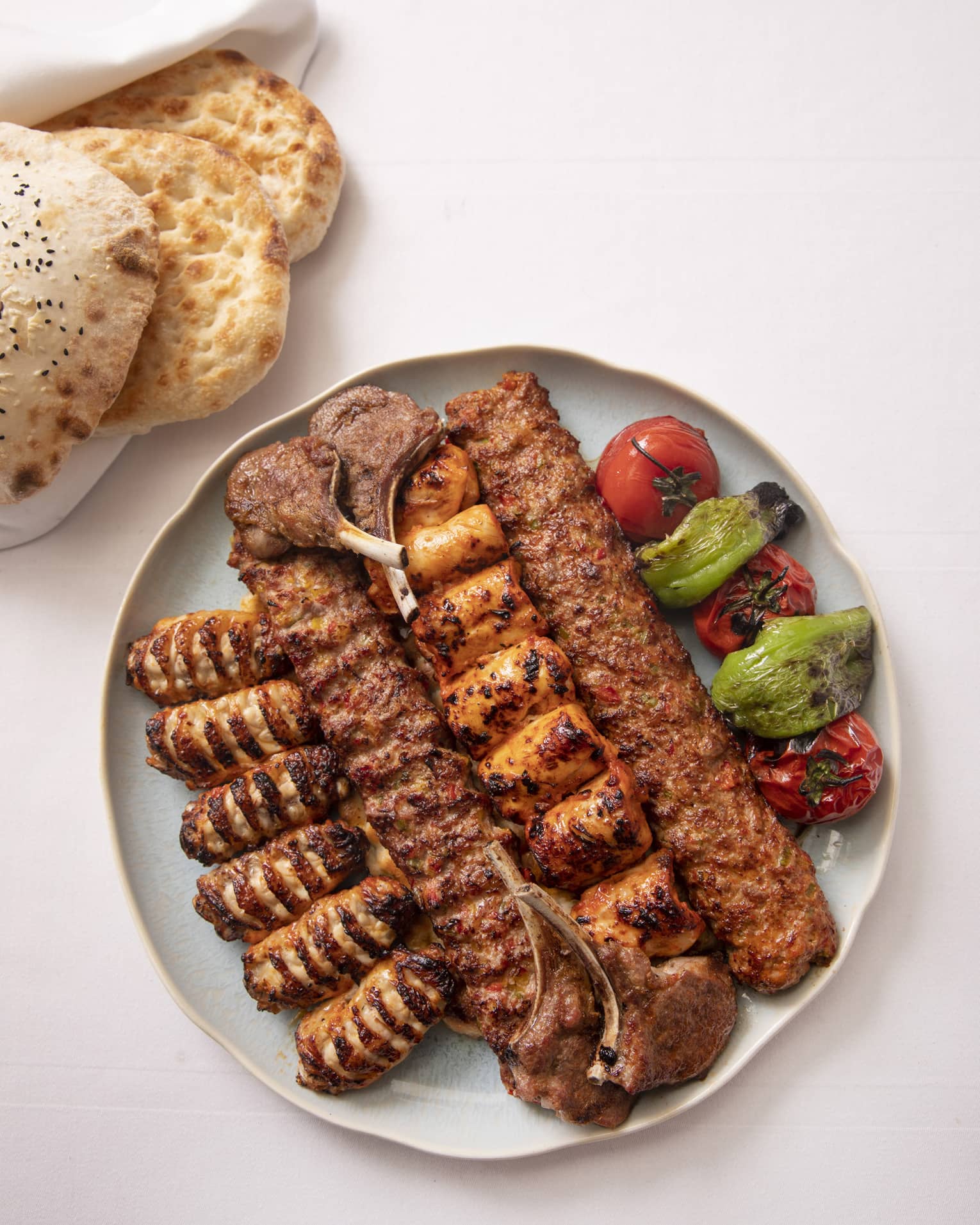 Grilled meat skewers and vegetables on round plate beside flatbread