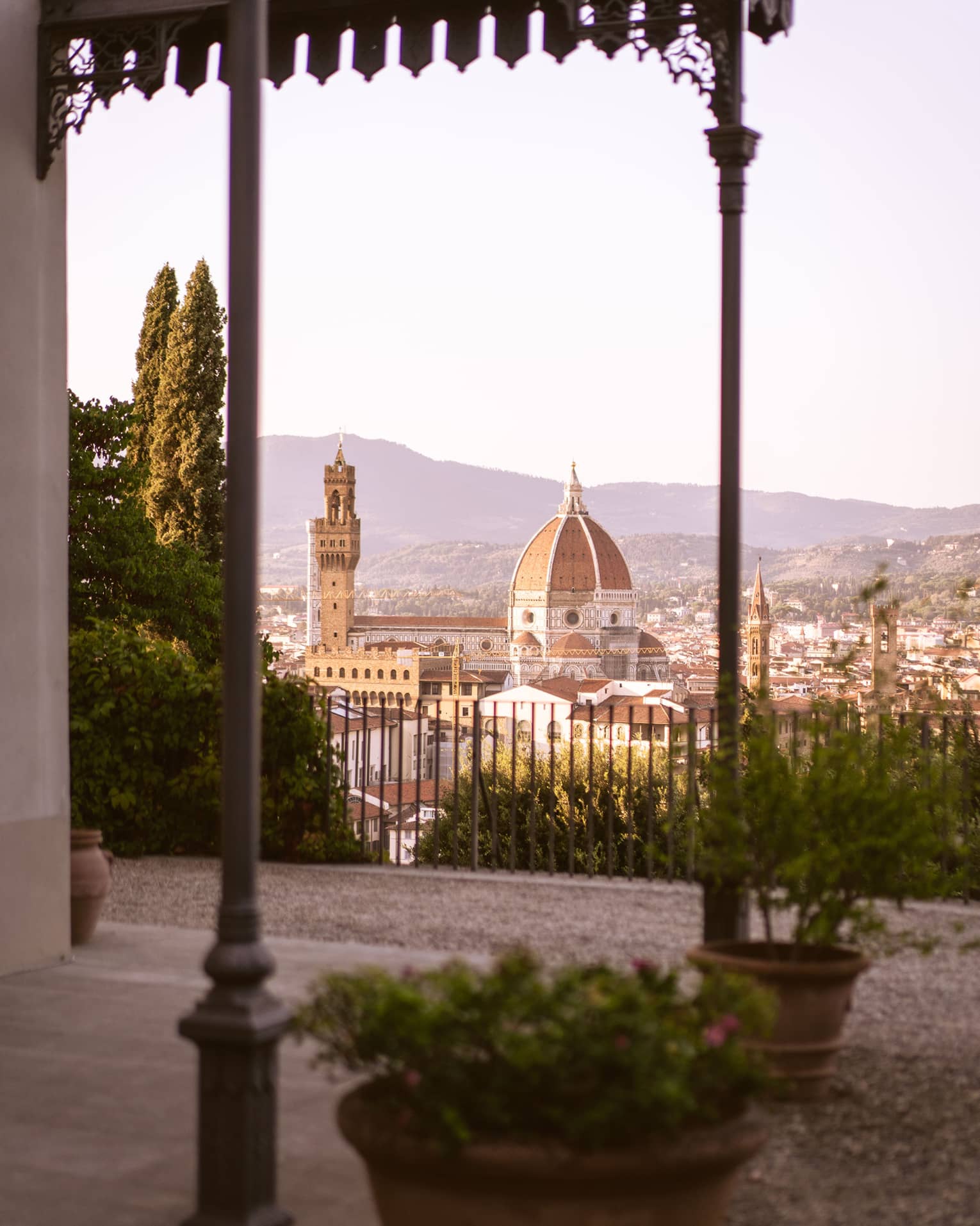 Distant view of the Florence Cathedral and the surrounding city, seen from a large, high-up fenced patio with potted plants.