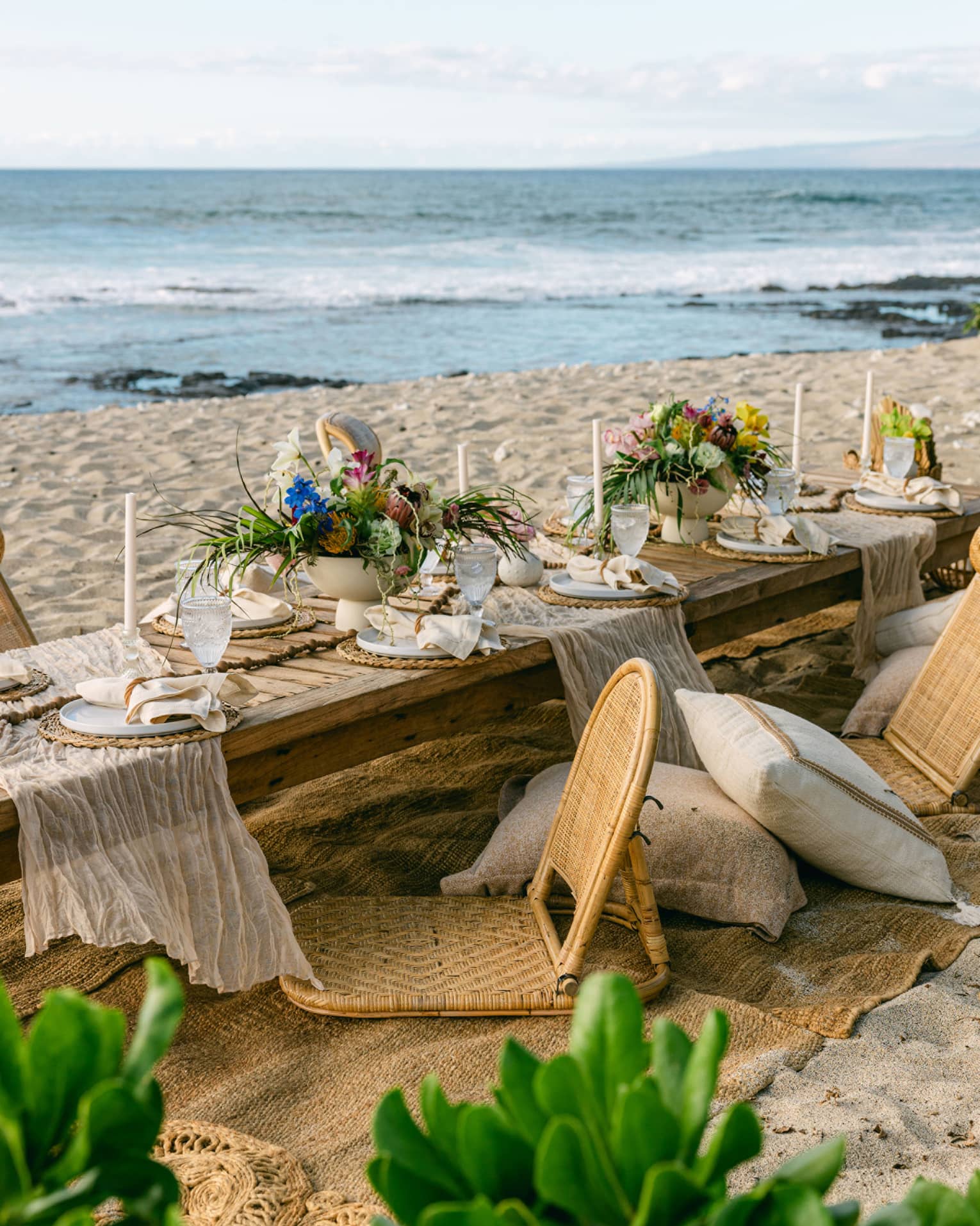 Low dining table set on the beach for an elaborate gourmet picnic, with floral arrangements and candle sticks