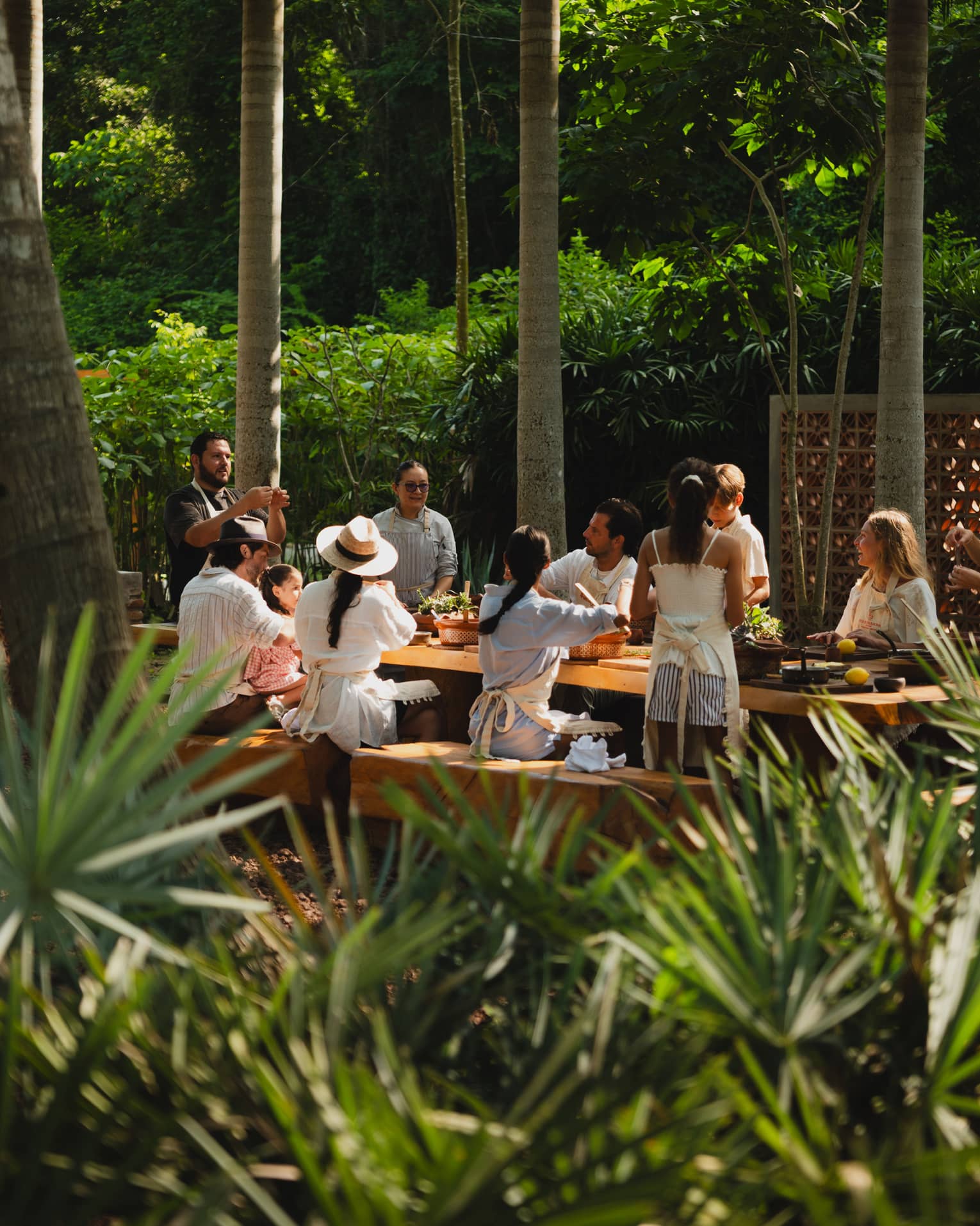 People seated around a long outdoor dining table set among palm trees
