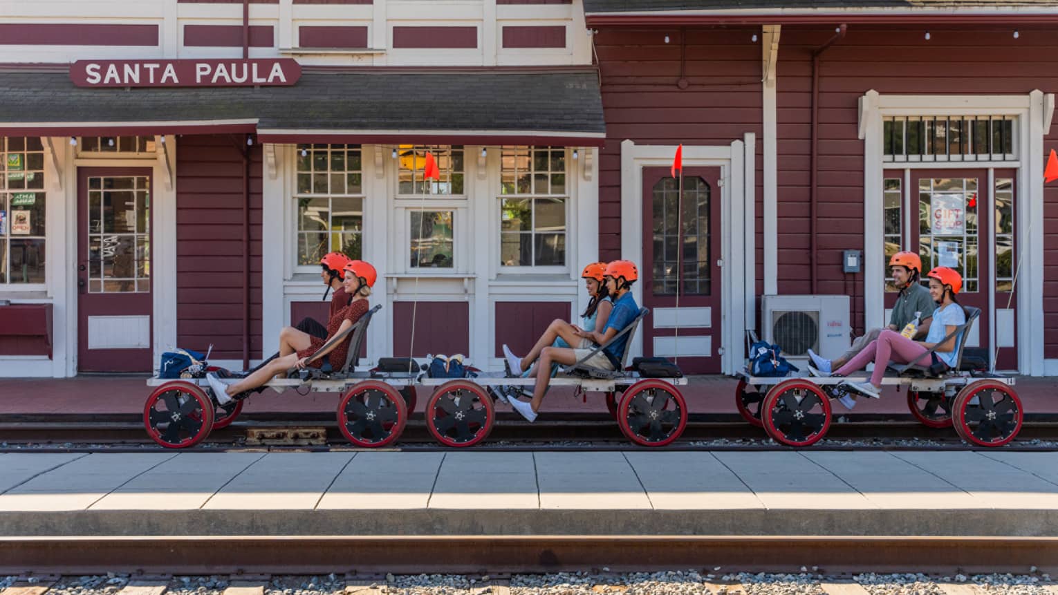 Six guests wearing helmets and riding railbikes on a track outside