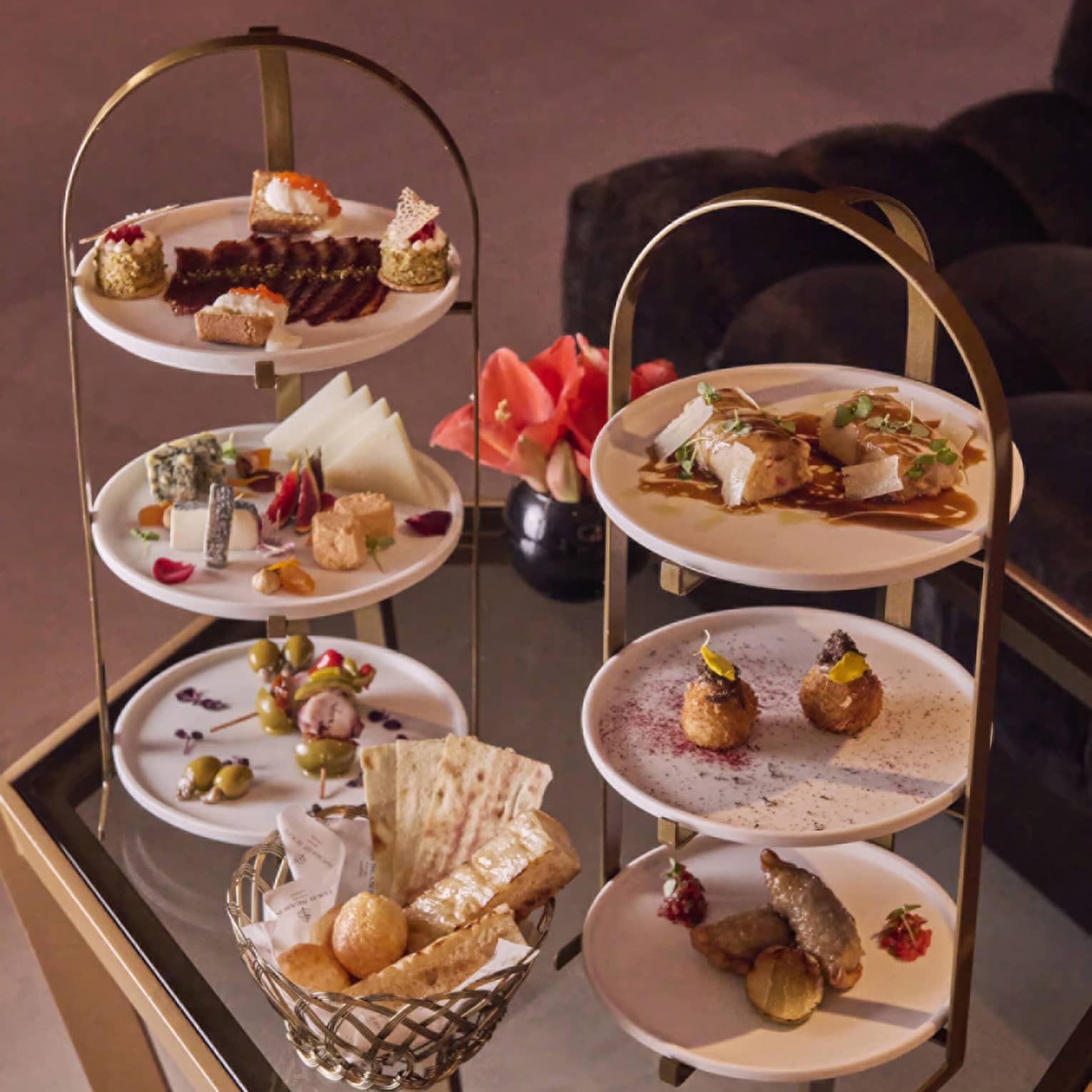 Tiered white and gold trays with a variety of savoury food of meats, cheese, olives, bread and pastries laid out on a table.