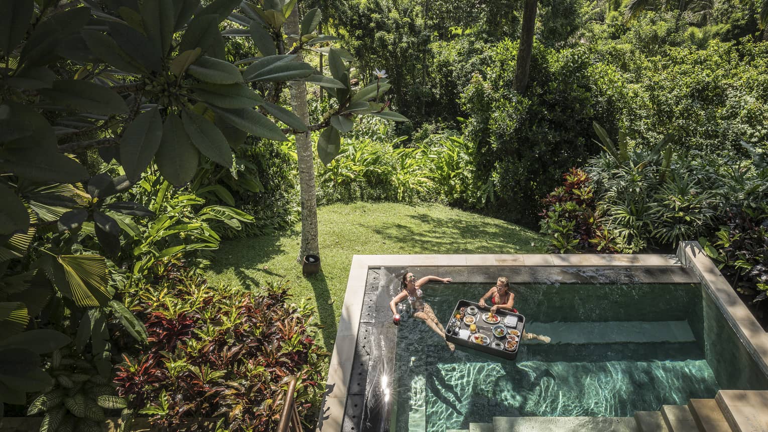 A couple lounges in the pool with breakfast on a floating tray 