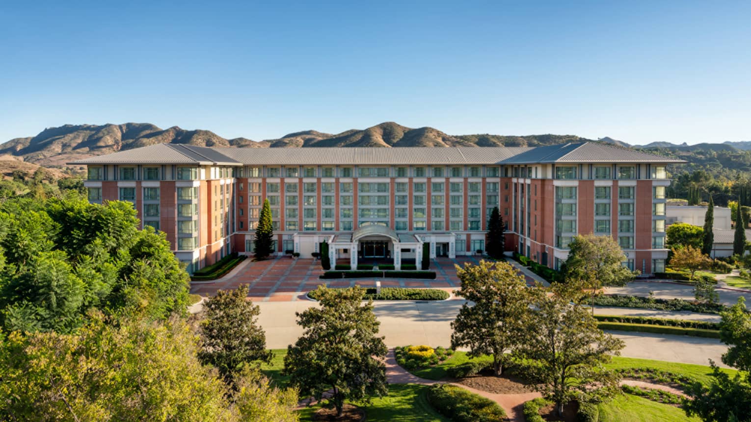 Exterior of hotel with trees in front of the building and mountains in the background.