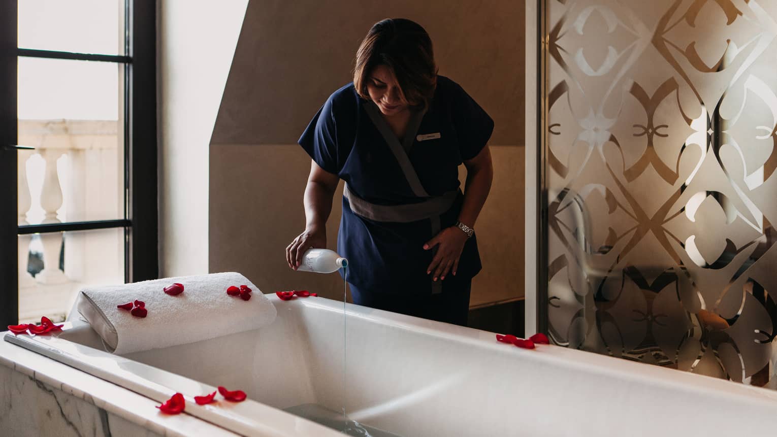 Hotel staff pours liquid into spa tub with rose petals