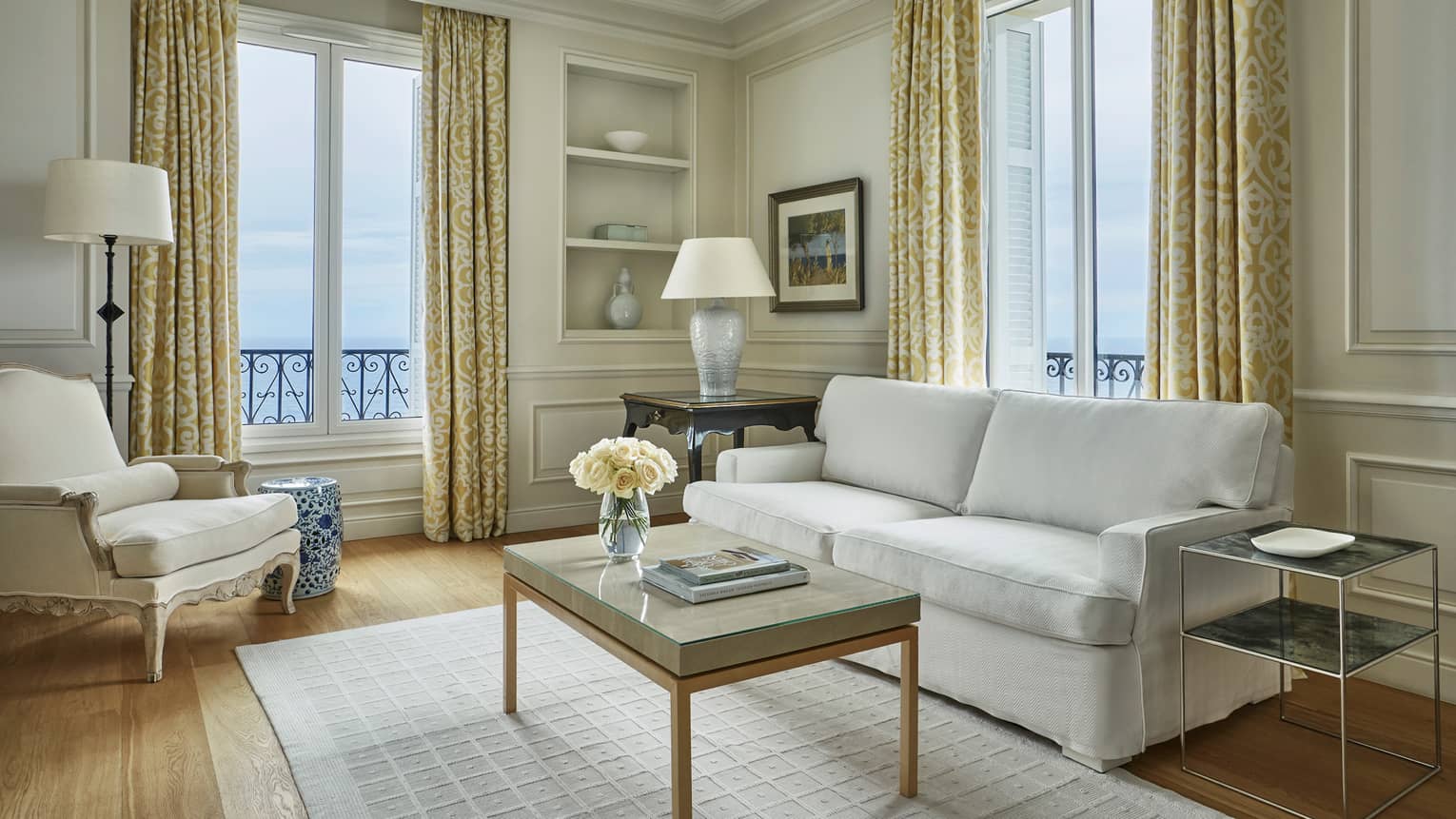 Modern white sofa, armchair, rug, table with books, flowers, corner windows