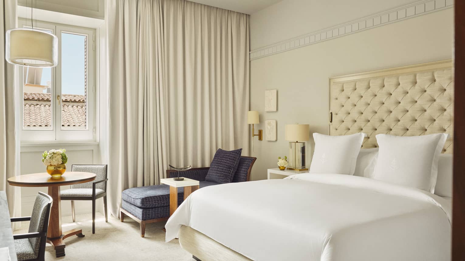 Luxury hotel room with king bed, upholstered cream-coloured headboard, cream-coloured curtains and window
