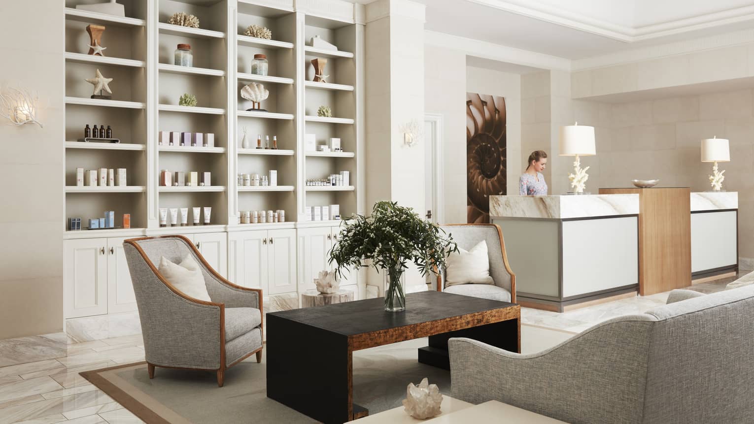 The lobby of a Spa with products on shelves, chairs, a coffee table and a reception desk.