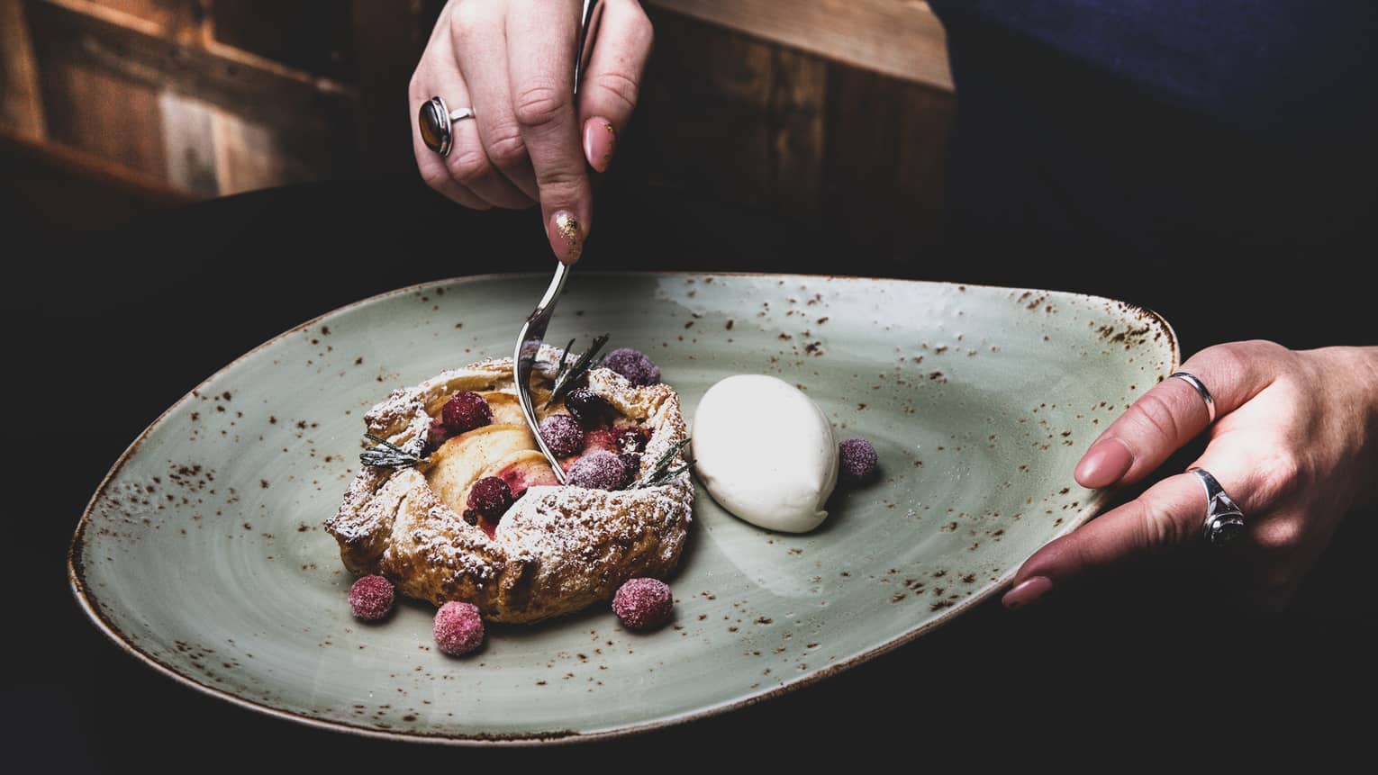 A person dips a spoon into a strudel filled with fruit.
