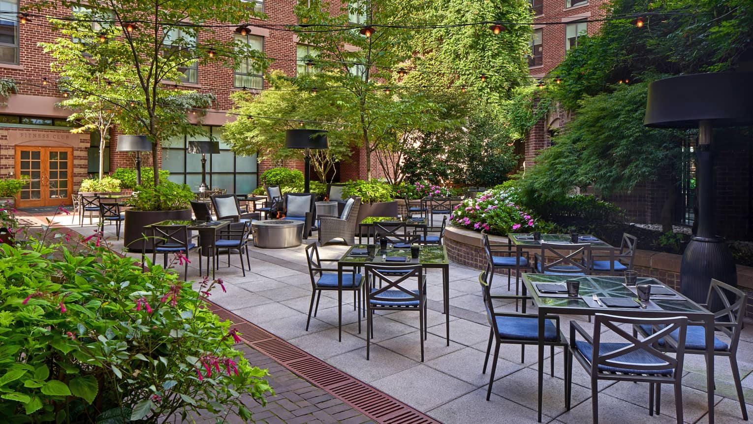 An outdoor eating area with metal chairs and glass tables surrounded by plants.