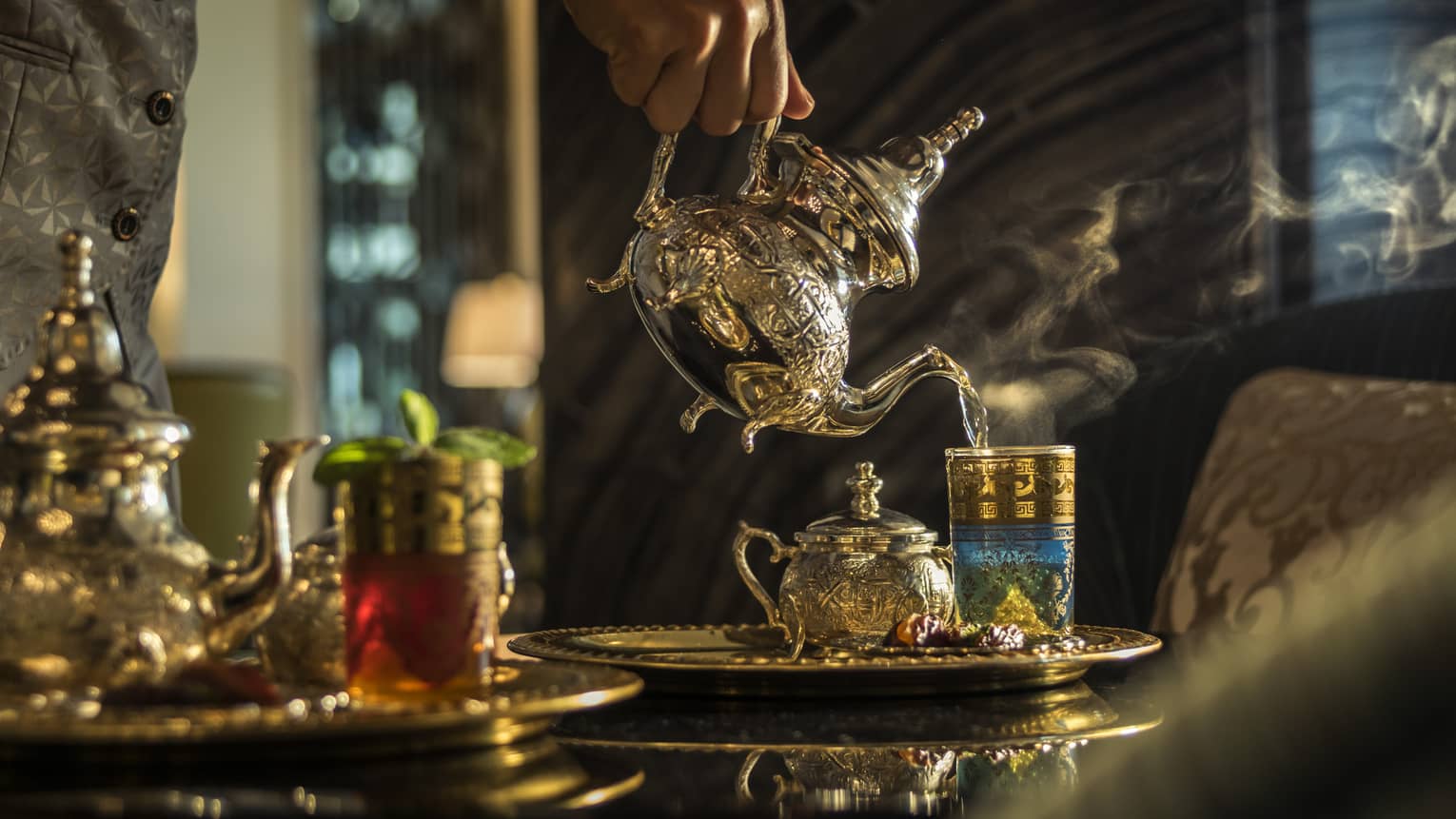 Hand pouring tea from Moroccan-style teapot into glass on tray