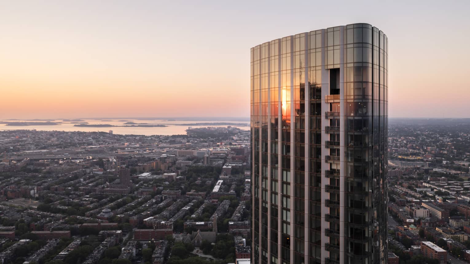 The exterior of a glass and steel skyscraper looking over a city with water in the distance.