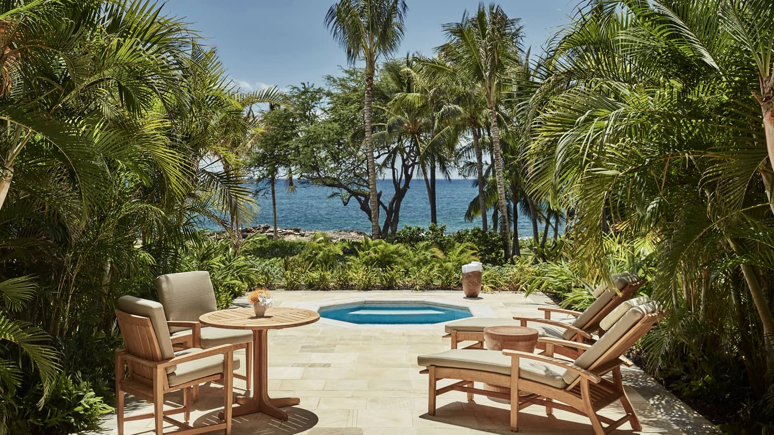Deluxe Jacuzzi Room patio with chairs around octagon-shaped jacuzzi tub on palm-lined patio