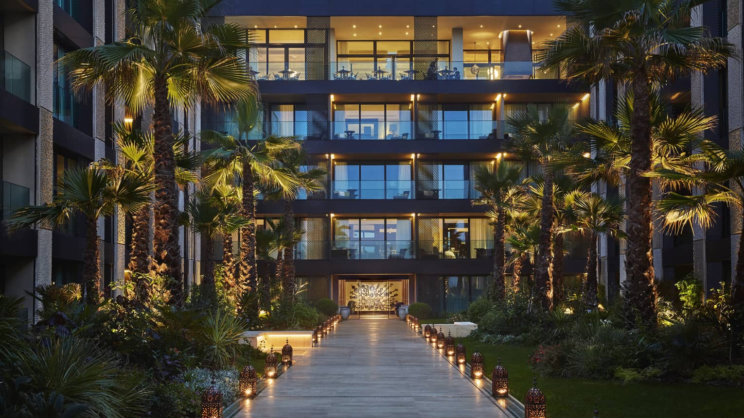 Lanterns. palm trees with lights along walkway under Four Seasons Hotel Casablanca building at dusk