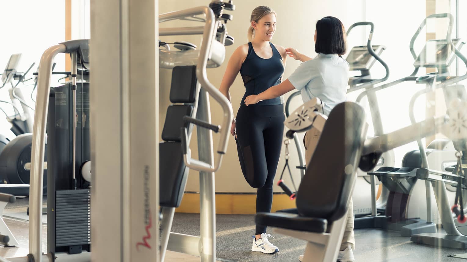 Personal trainer helps woman with pose by weights equipment in fitness room