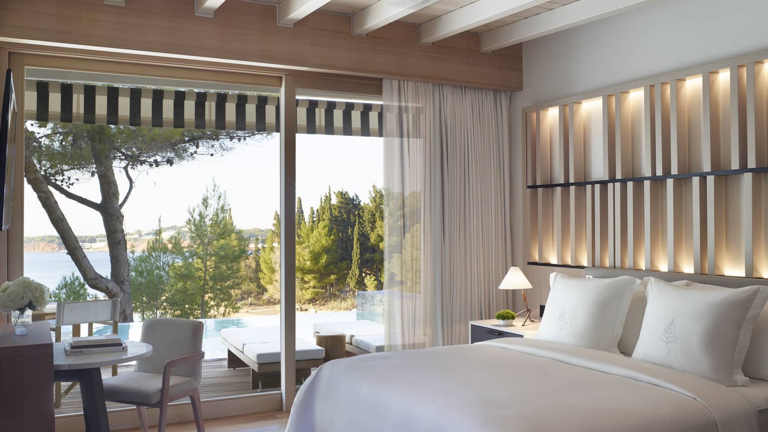 Bungalow Bedroom Sea View with Pool, white king bed, floor-to-ceiling window overlooking pool, desk and chair, backlit wall