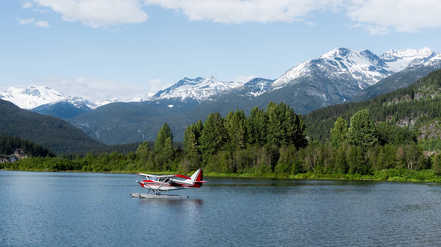 A small plane on a lake surrounded by forest with mountains in the background.
