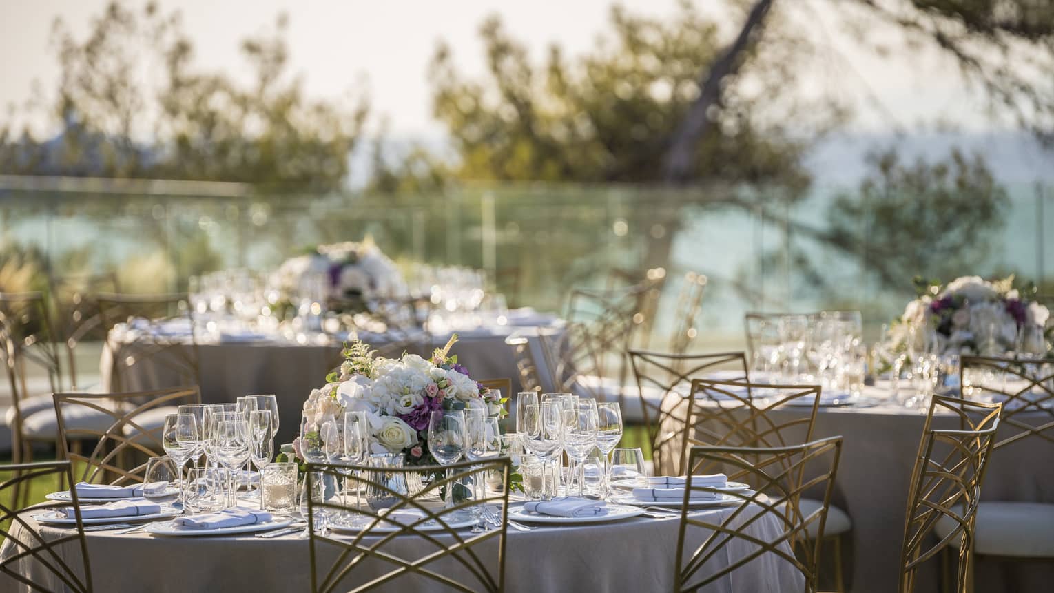 Romantic outdoor table setting with flowers, wine glasses and white linens overlooking trees and ocean